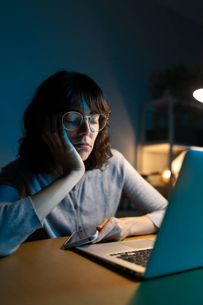 istock Tired young woman working late at night on laptop and tablet 2201020493