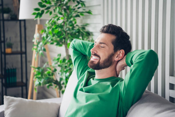Young man smiling and relaxing in a comfortable home environment with an indoor plant and natural daylight
