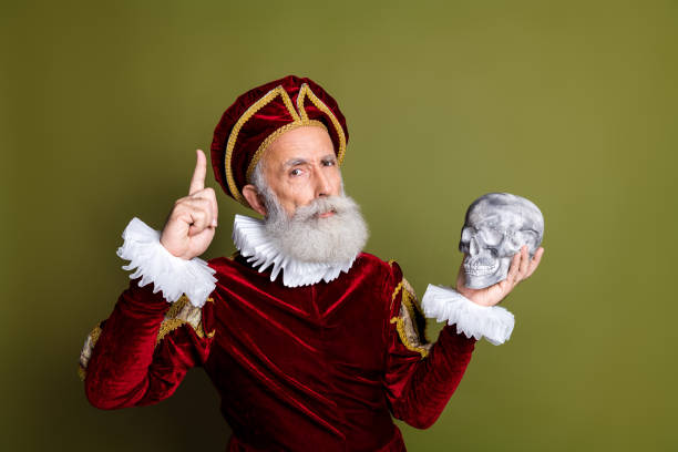 istock Senior man in renaissance costume holding a skull, reflecting on mortality, dramatic expression, khaki background 2201022180