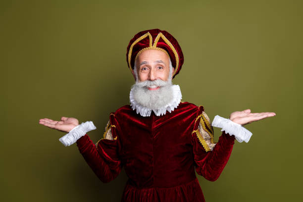 istock Senior man in royal renaissance attire presenting with hands raised against khaki background 2201022194