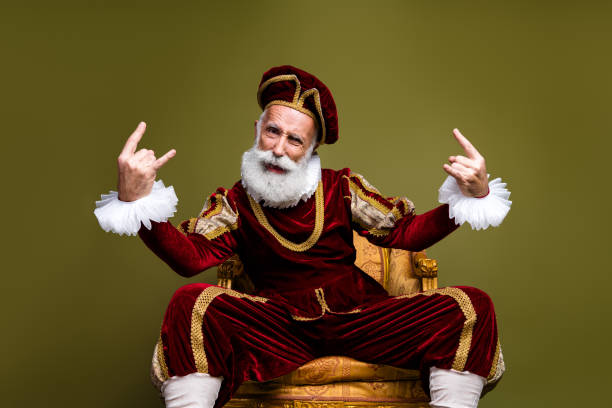 istock Elderly man dressed in royal medieval attire posing modern gestures on khaki background 2201022259