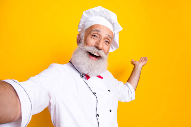 istock Cheerful senior chef with a white uniform posing against a bright yellow background 2201023039