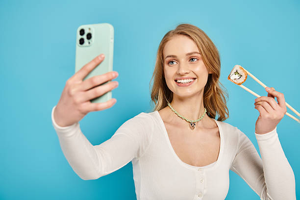istock Capturing joy through a selfie while enjoying sushi against a vibrant blue backdrop 2201029438