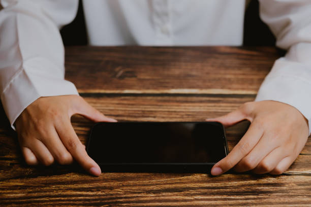 istock Hands Holding Smartphone on Wooden Table Background, Focused View 2201031051