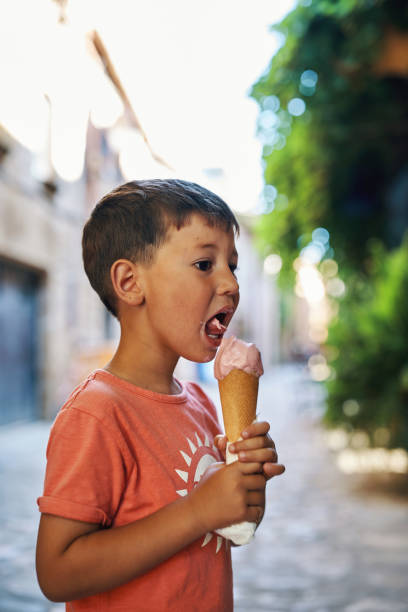 istock Young boy licking ice cream cone on a warm day in a rustic street 2201031126