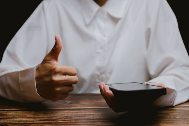 istock Person Giving Thumbs Up While Holding Smartphone on Wooden Table 2201031138