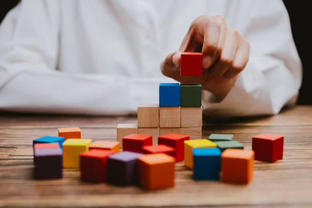 istock Colorful Building Blocks Stacked on Wooden Table with Child's Hand 2201031186
