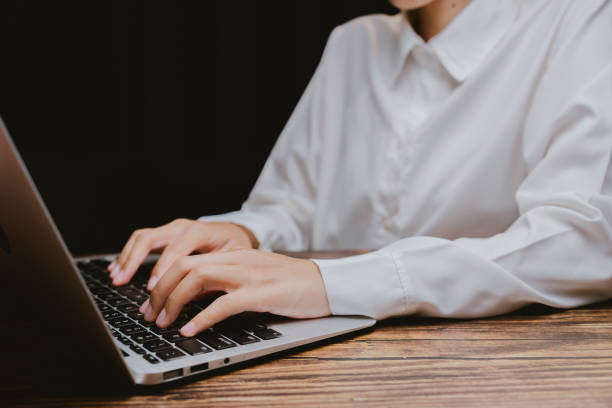 Person Typing on Laptop with Hands in Focus on Wooden Surface