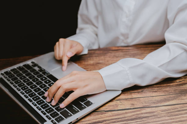 istock Person in White Shirt Typing on Laptop with Wooden Table Surface 2201031319