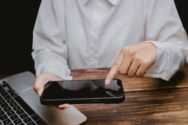 istock Person Using Smartphone While Working on Laptop at Wooden Desk 2201031355