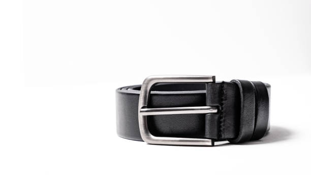 istock Twisted black leather belt with matted metal buckle isolated on white background. Fastened fashionable unisex, man or woman accessory for trousers, jeans, dress. Male luxury strap. Haberdashery goods 2201034020