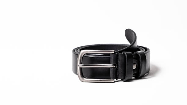 istock Twisted black leather belt with matted metal buckle isolated on white background. Fastened fashionable unisex, man or woman accessory for trousers, jeans, dress. Male luxury strap. Haberdashery goods 2201035434