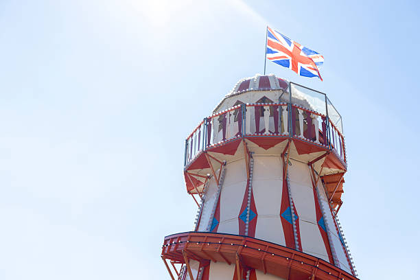 Medium low-angle shot of the top of a helter-skelter on a sunny day at a fairground in Newcastle-upon-Tyne, North East England. There is a British flag flying from the top.\n\nVideos similar to this scenario available.