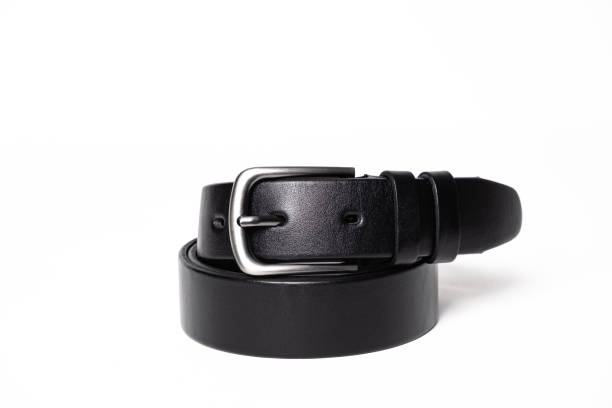 istock Twisted black leather belt with matted metal buckle isolated on white background. Fastened fashionable unisex, man or woman accessory for trousers, jeans, dress. Male luxury strap. Haberdashery goods 2201037491