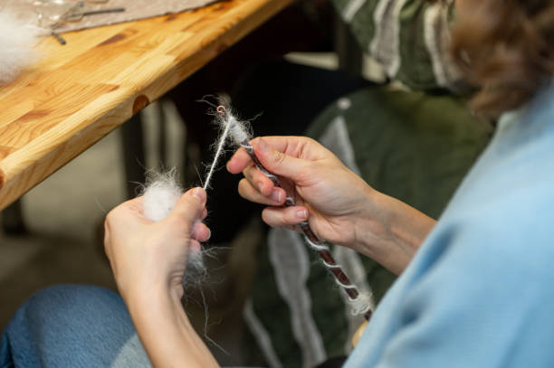 istock Female hands spinning wool yarn with drop spindle in crafting session 2201041307