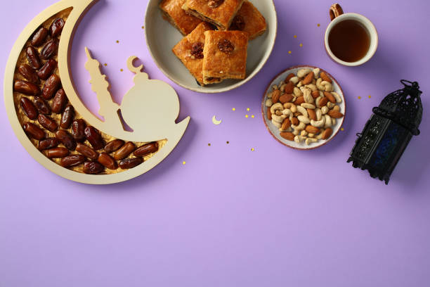 istock Celebrate Ramadan with a traditional setup featuring dates, mixed nuts, pastries, tea, and a decorative lantern on a purple background 2201049623