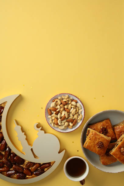 istock Ramadan celebration concept. Bright Ramadan food arrangement with dates, nuts, baklava, and cup of tea on a yellow background 2201049727