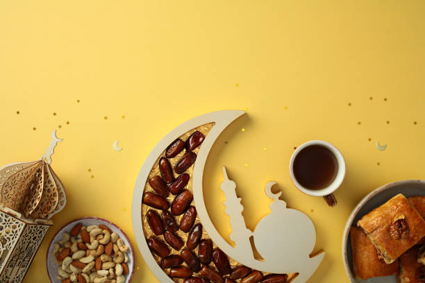 istock Ramadan celebration concept. Dates in a crescent moon tray, baklava on a plate, mixed nuts, and a decorative lantern on a yellow background with star confetti 2201049849