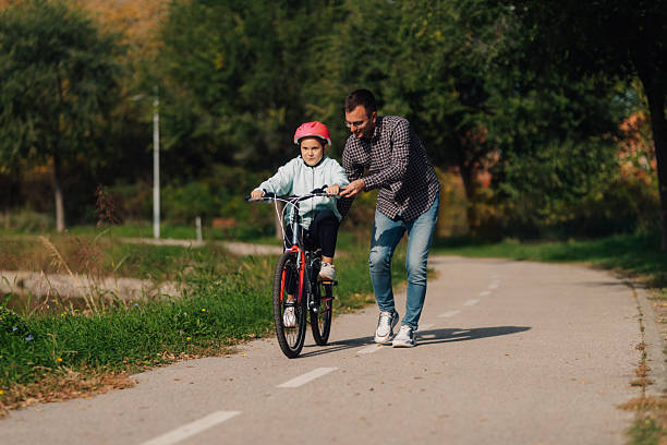istock Father teaching daughter riding bicycle in park during fall 2201051288