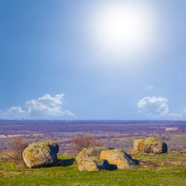 green stony field under a sparkle sun on blue cloudy sky background