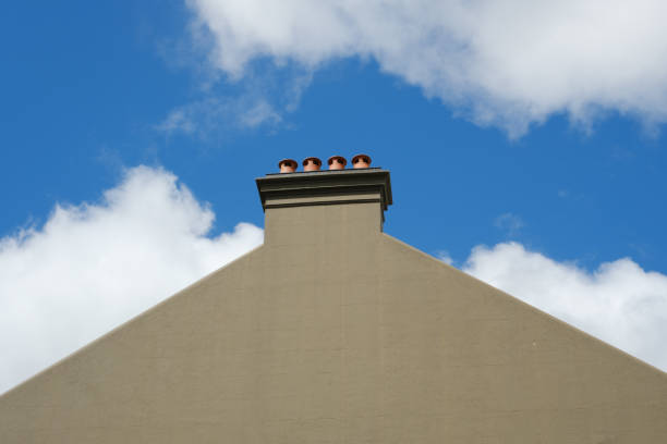 Close-up on a side wall of a building with chimney and a cloudy blue sky beyond.