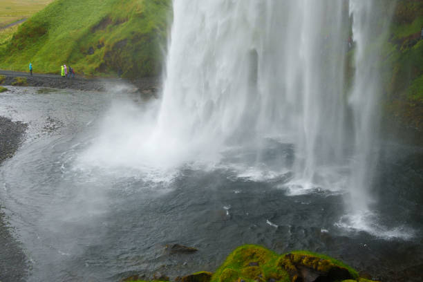 Tourists admiring the stunning seljalandsfoss waterfall as it cascades into a rocky pool, creating a mesmerizing misty spectacle in the breathtaking icelandic landscape