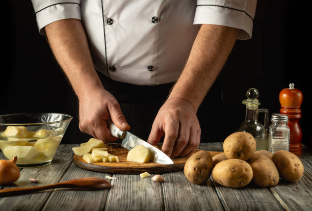 istock A skilled chef chops fresh potatoes on a wooden board, surrounded by an assortment of ingredients. The cozy kitchen ambiance enhances the culinary artistry being showcased 2201058329