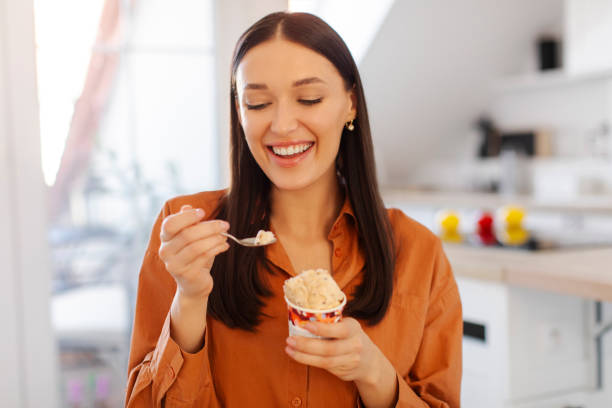 istock Fun and sweets. Happy lady eating ice cream and smiling, sitting in kitchen interior, having time for dessert 2201058560