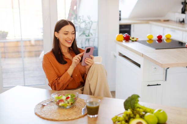 istock Happy woman using cellphone in kitchen while having dinner, sitting at table with bowl of fresh salad and texting on mobile phone, copy space 2201058819