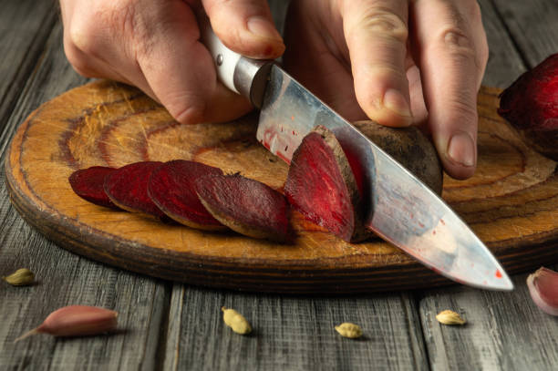 istock Hands skillfully slice through vibrant red beets on a rustic wooden cutting board. The warm kitchen light casts a cozy atmosphere while prep for a delicious meal begins 2201059301