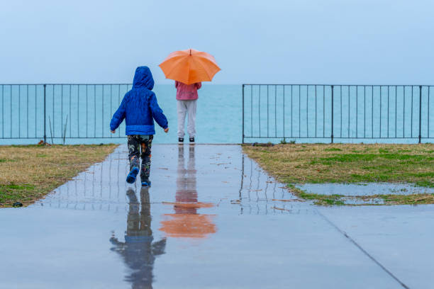Siblings holding an umbrella watching the sea in rain