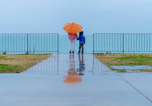 Siblings holding an umbrella watching the sea in rain