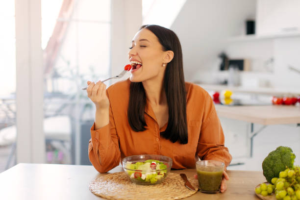 istock Young woman enjoying fresh vegetable salad, holding fork with tomato, eating tasty lunch while sitting in kitchen interior, copy space 2201064806