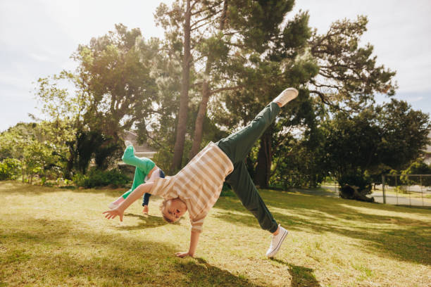 Two playful children are seen performing cartwheels in a scenic park. The sunny day provides a cheerful atmosphere, highlighting the joy and energy of youth engaging in lively outdoor activities.