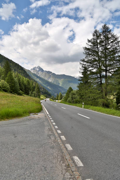 istock Scenic mountain road winding through lush green valleys under a dynamic sky 2201073960