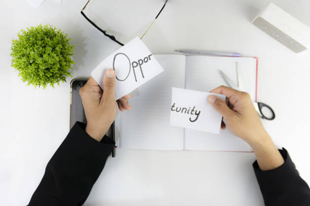 istock The word Opportunity is cut in half and held above an open notebook on a white desk. 2201076333