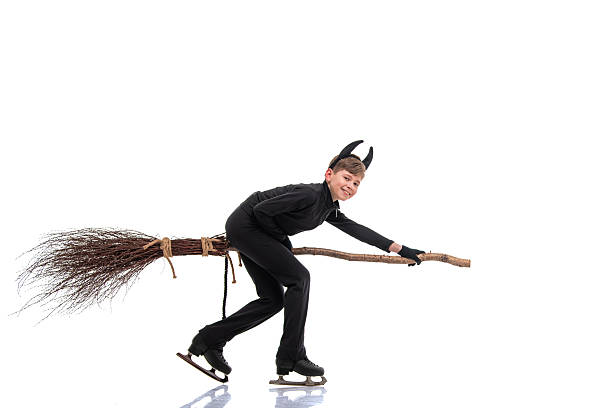Young figure skater in a devil costume with a broomstick performing on the ice rink during Halloween