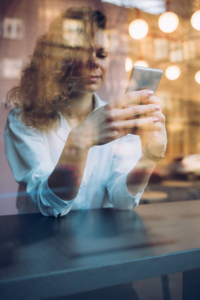 istock A woman is sitting at a table looking at her cell phone 2201084471