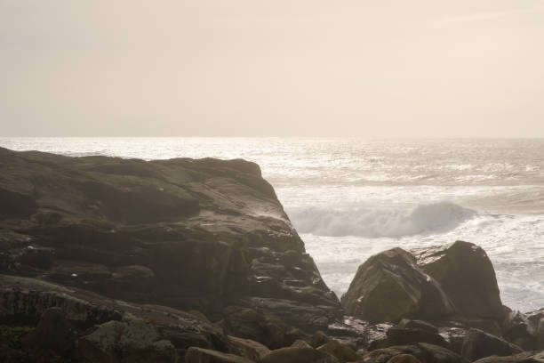 Dramatic ocean waves crashing against a rocky coastline during a hazy sunset