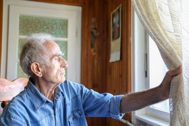 Nosy Senior Man at Home Curiously Peering Through the Window, Observing the Neighborhood with Intense Focus