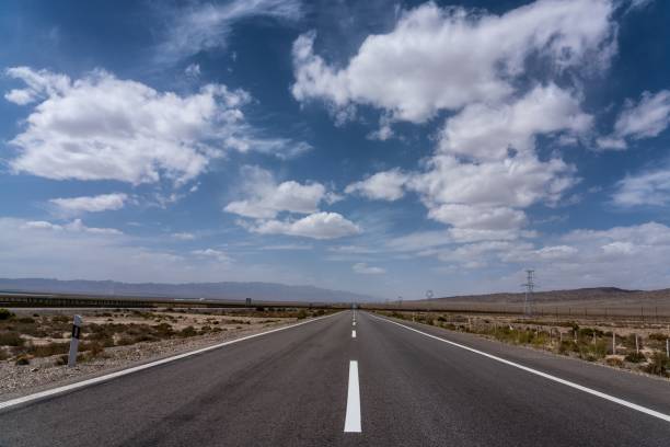 istock Deserted highway stretching into the distance under a blue sky with fluffy clouds 2201093897