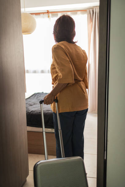 istock Woman with suitcase standing by a window in a bright hotel room 2201098232