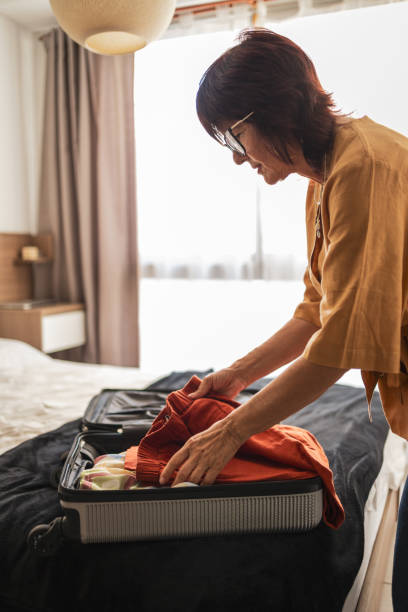istock Person packing clothes into a suitcase on a bed by a window 2201098247