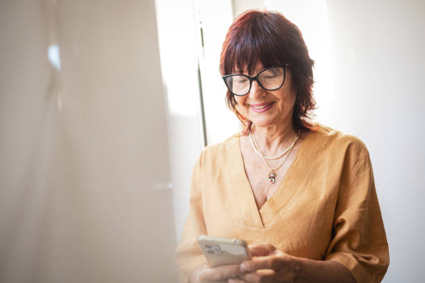 istock Smiling Senior Woman Using Smartphone Indoors During Bright Daylight 2201098285