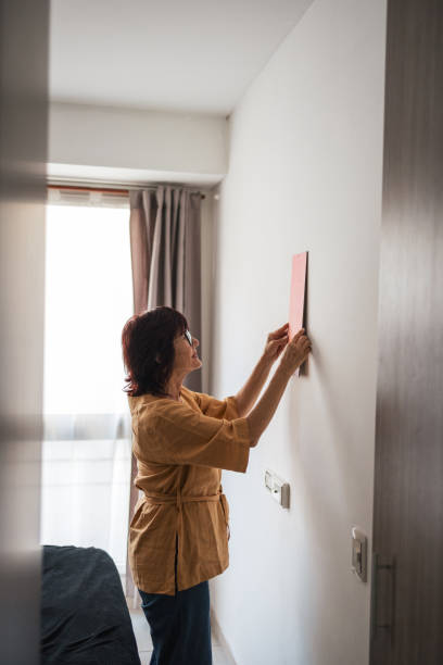 istock Woman decorating a wall with a decorative item in a neat bedroom 2201098290