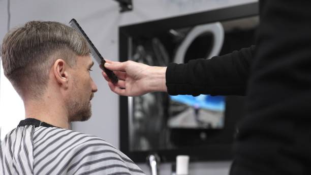 istock Barber carefully combing hair, client wearing protective cape, preparing for precision styling inside sleek contemporary barbershop setting 2201098757
