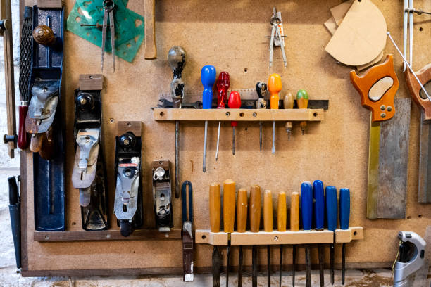 Carpentry tools are on the wall of a workshop. These include crew drivers, chisels, saws and  planers in a variety of  sizes.