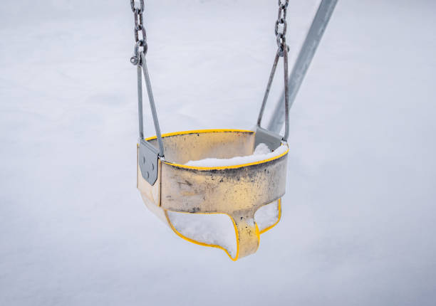 Close up of yellow toddler swing set seat. Closed playground due to blizzard condition or winter snow fall. Selective focus.