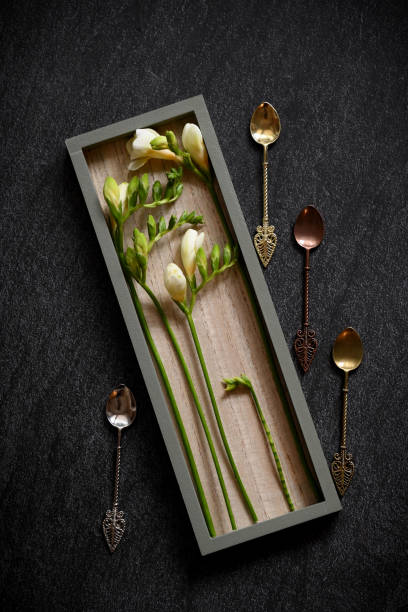 composition of white freesias arranged in a rectangular wooden frame on a dark background, perhaps a dark stone