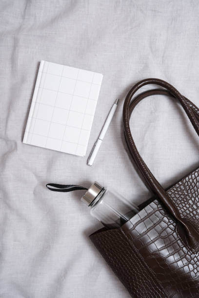 istock This stylish accessories flat lay of trendy dark brown bag, a chic notebook, a white pen, a water bottle on grey fabric background. 2201109331